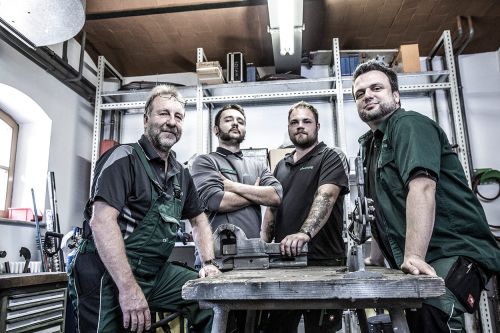 Ein Team von vier Handwerkern steht selbstbewusst in einer Werkstatt, spezialisiert auf Heizung und Sanitärtechnik.
