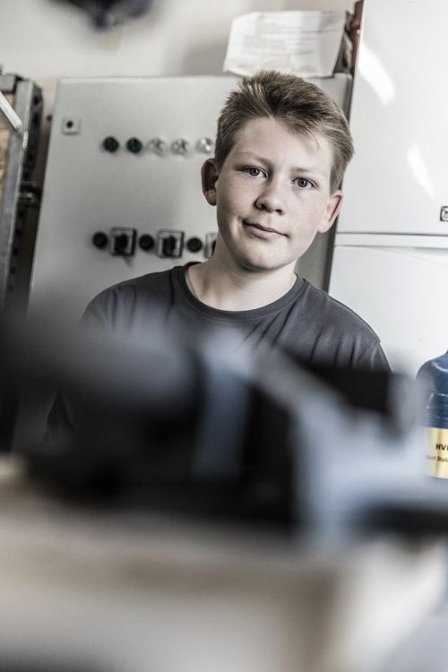 Ein Junge steht vor einer Schalttafel für Heiztechnik in einem lichtdurchfluteten Raum.