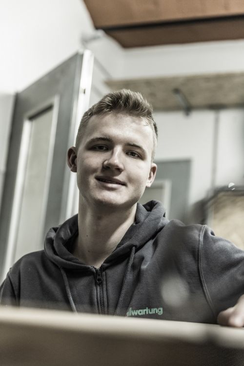 Ein junger Mann in Arbeitskleidung lächelt im Bereich Klimatechnik in die Kamera. | © Das Kraftbild