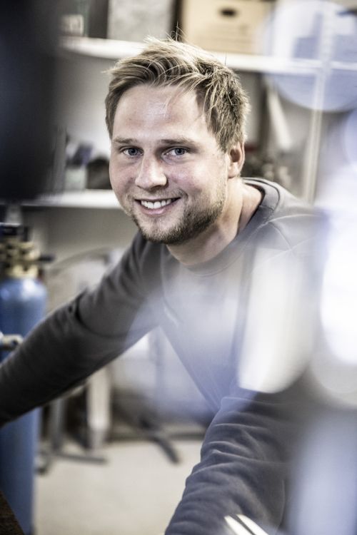 Ein lächelnder Handwerker arbeitet an einer Heizungsbauanlage, umgeben von Werkzeugen für Heiztechnik.