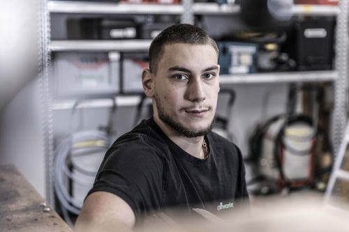 Ein Mann sitzt in einer Werkstatt, umgeben von Werkzeugen für Sanitär- und Heiztechnik, und wirkt konzentriert.