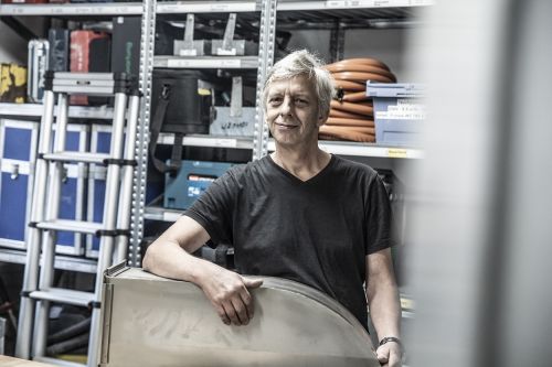 Ein Mann steht in einer Werkstatt, umgeben von Werkzeugen und Materialien für Klimatechnik.