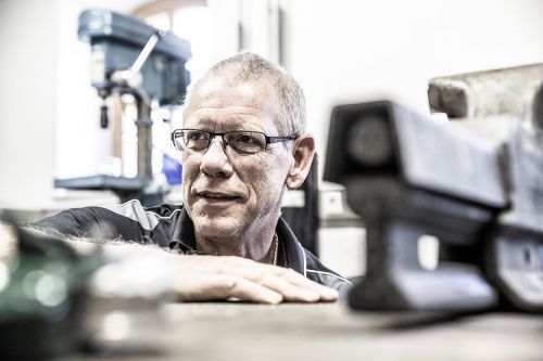 Ein Mann arbeitet konzentriert in einer Werkstatt an sanitären Anlagen, umgeben von Werkzeugen und Maschinen.