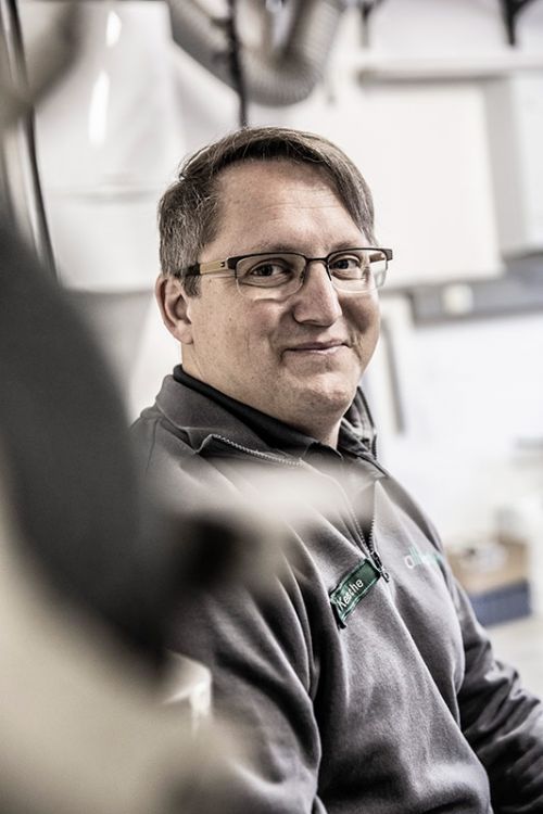 Ein Mitarbeiter lächelt in einer Werkstatt, während er an einer Sanitärinstallation arbeitet.