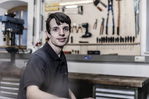 Ein junger Mann sitzt in einer Werkstatt, umgeben von Werkzeugen für Sanitär- und Heiztechnik.