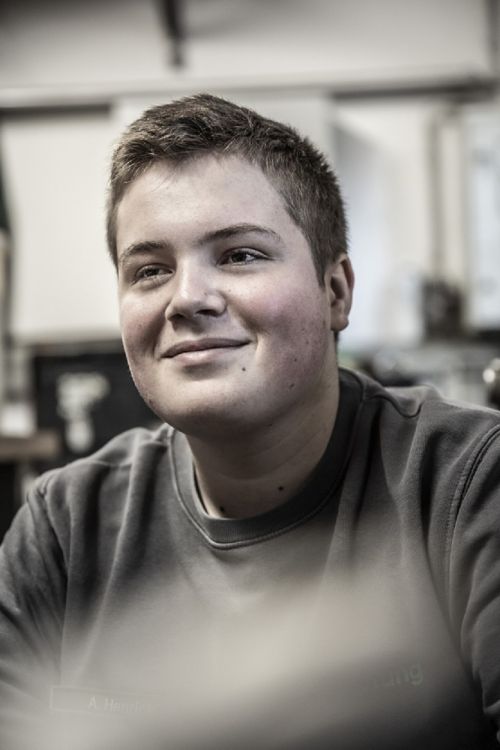 Ein junger Mann lächelt in einer Werkstatt, bereit für eine Aufgabe in der Klimatechnik.