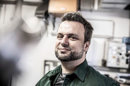 Ein lächelnder Anlagenmechaniker in München arbeitet in einer Werkstatt für Heiztechnik.