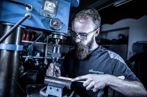 Ein Mann arbeitet konzentriert in einer Heizungsbau-Werkstatt an einer Bohrmaschine, um Heiztechnik-Komponenten herzustellen.