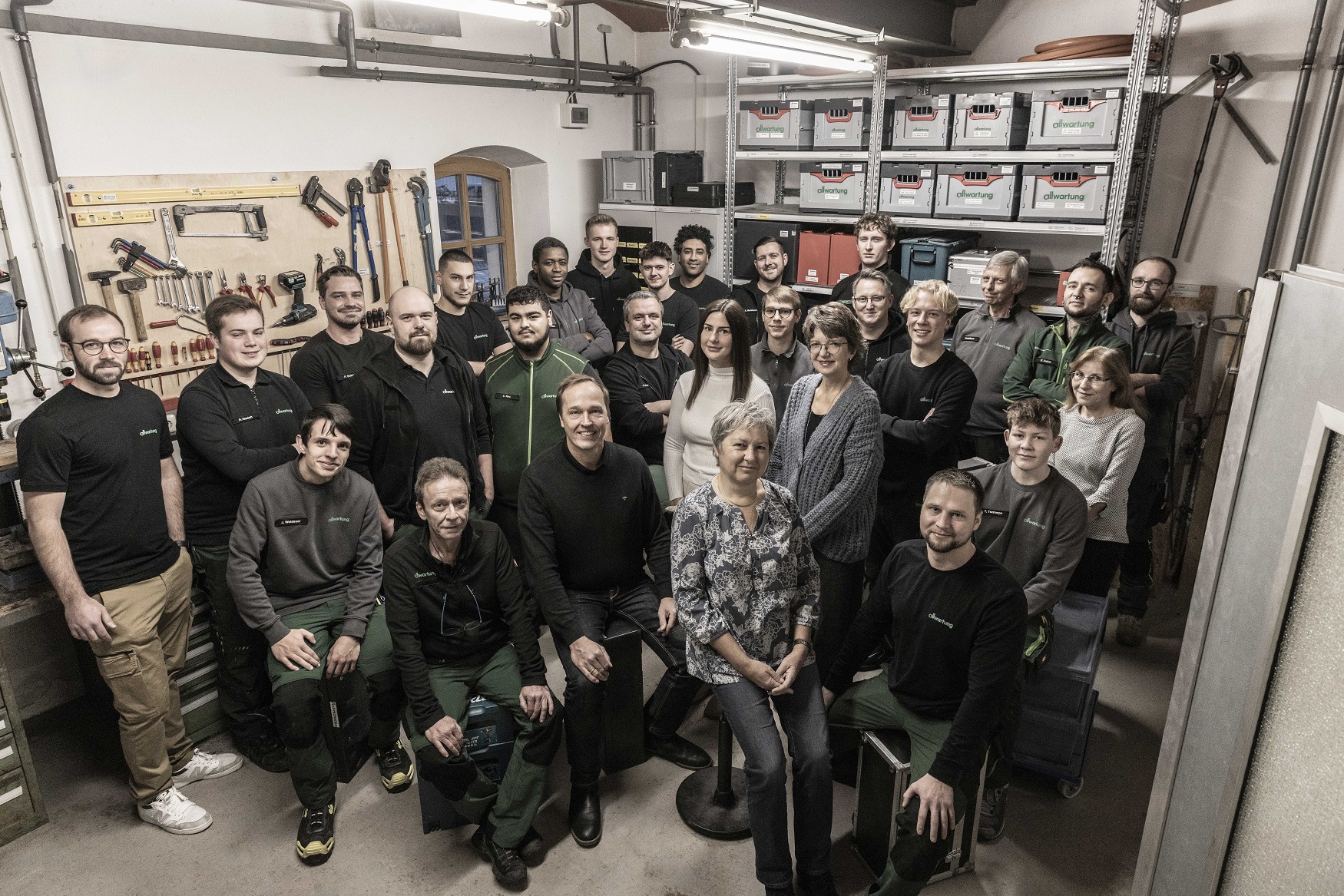 Eine Gruppe von Mitarbeitern posiert stolz in einem Lagerraum für Heiztechnik, umgeben von Werkzeugen und Regalen.