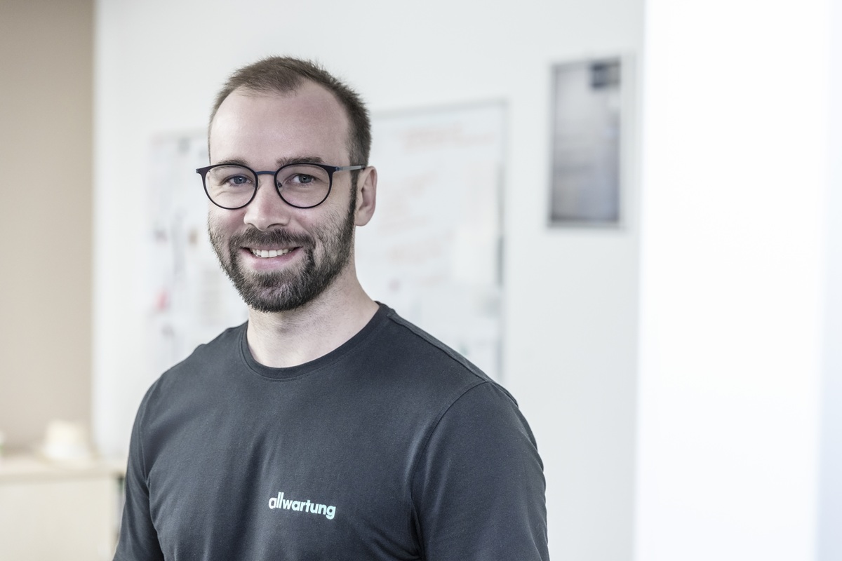 Ein lächelnder Mann in einem dunklen T-Shirt steht in einem hellen Raum, der mit lüftungstechnik ausgestattet ist.