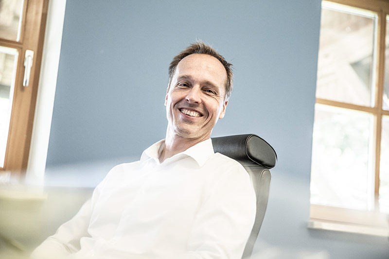 Ein lächelnder Mann sitzt entspannt im Büro und strahlt Vertrauen in den Bereichen Heiztechnik und Klimatechnik aus.