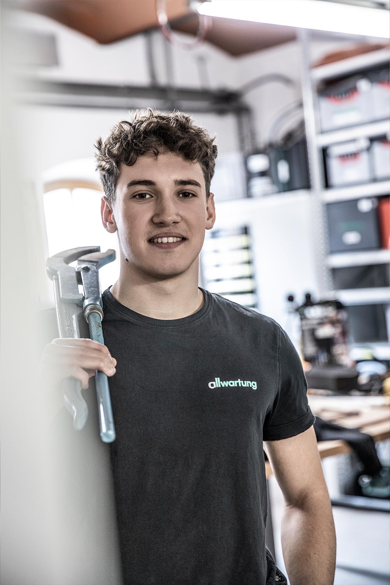 Ein junger Mann in Arbeitskleidung hält einen großen Schraubenschlüssel und arbeitet im Bereich der Klimatechnik.