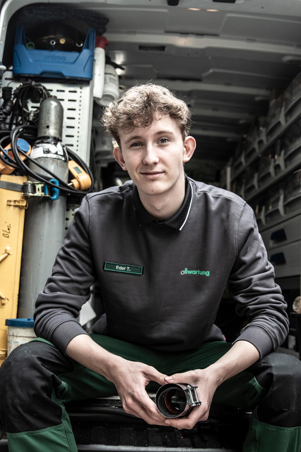 Ein junger Handwerker sitzt im Lieferwagen und hält ein Rohrstück für Heiztechnik in den Händen.
